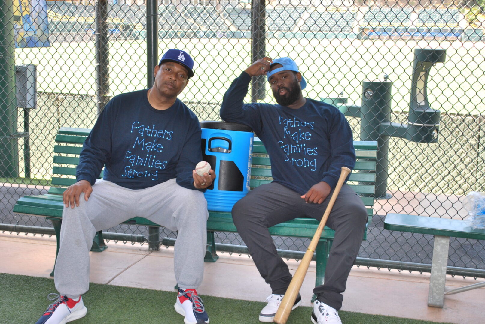 Two men sitting on a bench with baseball equipment.