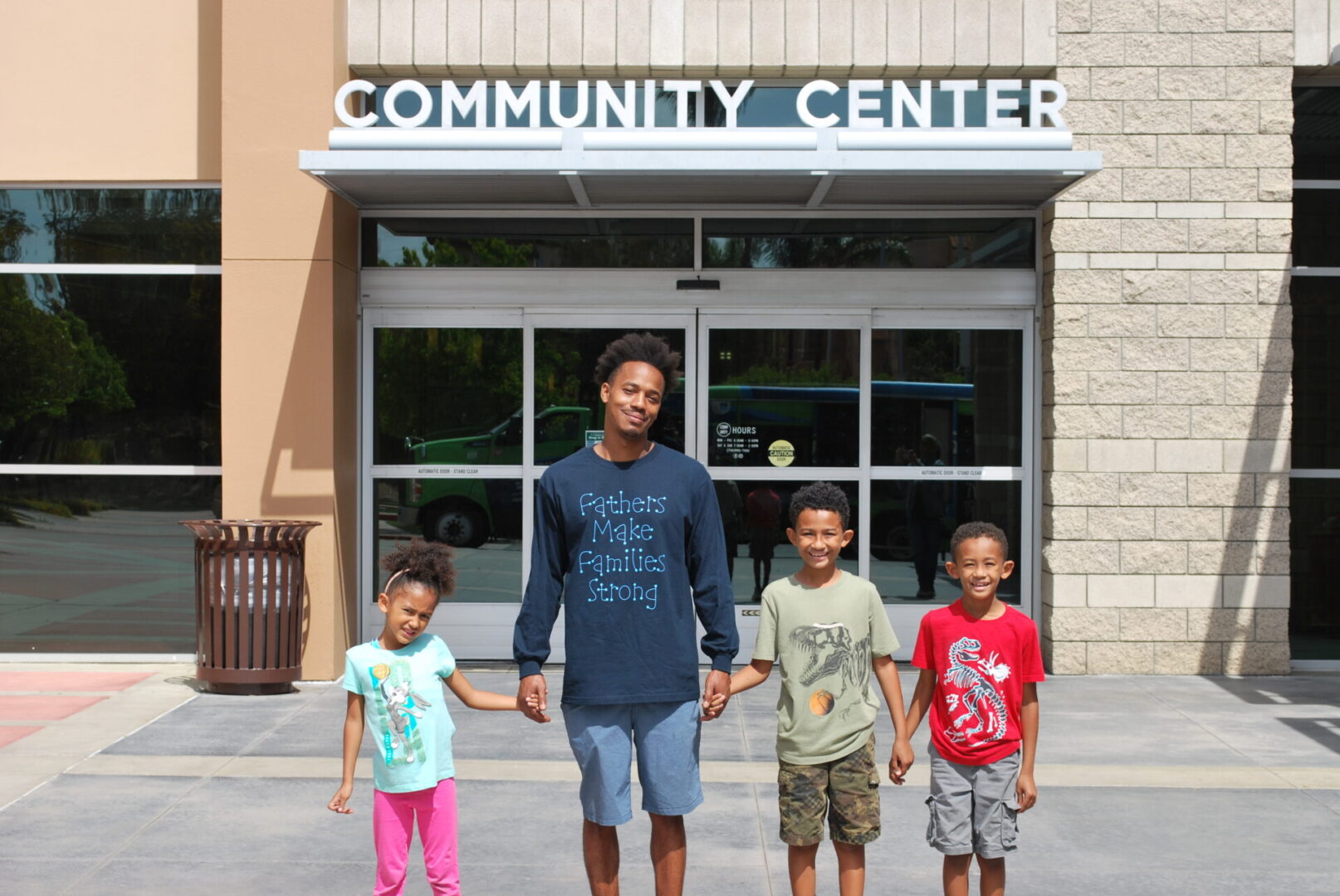 A man and two boys holding hands in front of the community center.